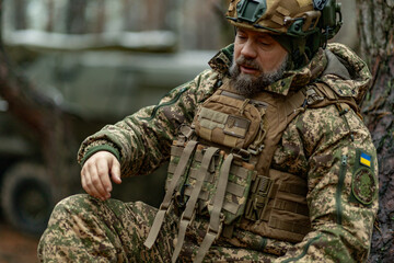 Fototapeta premium tired Ukrainian soldier sits down by a tree to rest after a battle.