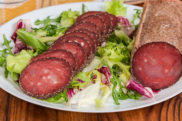 Partially sliced dry-cured sausage on leaf vegetables on dish
