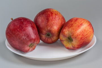 Red apples on a white dish on a gray background
