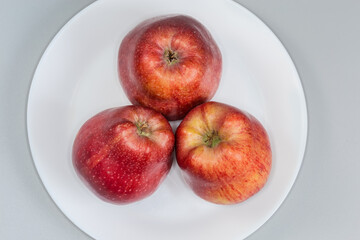 Red apples on white dish on gray background, top view