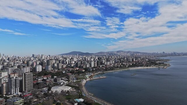 A stunning drone view of Caddebostan Coast Park on a sunny day. People enjoy the green spaces, walking paths, and seaside, while the blue waters of the Marmara Sea create a relaxing coastal atmosphere
