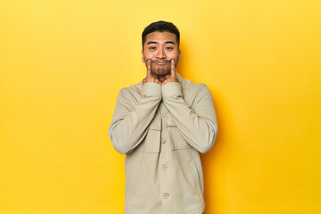 Fototapeta premium Asian man in stylish gray shirt on yellow studio doubting between two options.