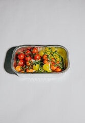 A tray of assorted fruits and vegetables, including tomatoes, oranges, and grapes. The tray is placed on a white background