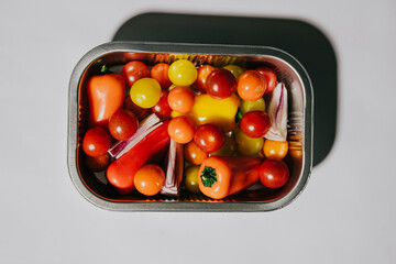 A metal container filled with a variety of vegetables including tomatoes, peppers, and onions. The container is placed on a white background
