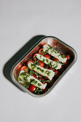 A tray of food with a variety of vegetables and cheese. The tray is silver and has a white background