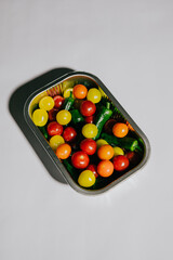 A tray of assorted fruits and vegetables, including tomatoes, peppers, and grapes. The tray is placed on a white background