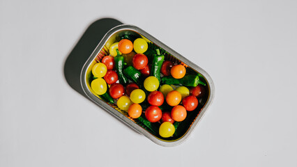 A tray of fruit is sitting on a white table. The tray contains a variety of fruits, including tomatoes, green peppers, and grapes. The fruits are arranged in a way that makes them look fresh