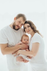 A happy young family mom dad and a small child smiling and kissing on a white isolated window background, a loving family threesome at home