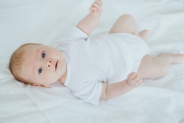 newborn baby boy smiling on a white bed at home, family with a small child, close-up, place for text