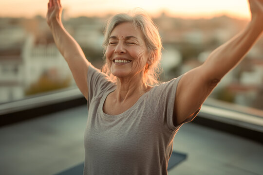 Elderly woman with arms raised smiling outdoors, promoting vitality, active lifestyle and aging with joy and empowerment.