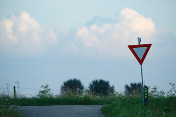 Yield sign stands prominently along a rural road under a dramatic sky near dusk