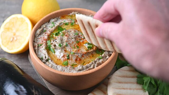 Dipping with pita bread in traditional baba ganoush in bowl on wooden table