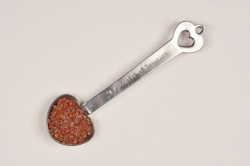 A top-down view of a silver heart-shaped spoon filled with red Hawaiian salt