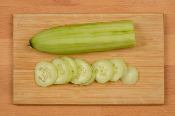 A top-down, flat-lay shot of a whole, peeled cucumber and a stack of sliced cucumber rounds on a...