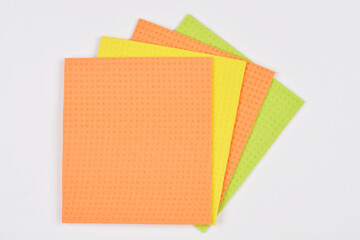 A top-down shot of a stack of four colorful sponge cloths, including orange, yellow, and green,...