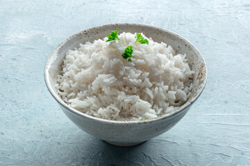 White rice, cooked. A bowl of boiled long grain rice, a simple side dish, with fresh parsley leaves