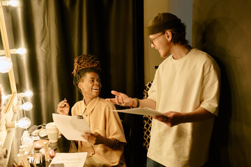 Two young adults collaborating on creative project in studio filled with warm lighting and artistic...