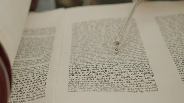 Close up of rabbi's hand holding a silver pointer and showing a line in a Torah scroll. Reading the great Jewish book of the Torah during prayer.