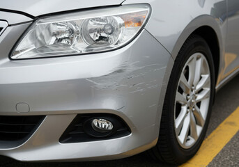 Closeup of car front bumper with scratches and scuff marks.