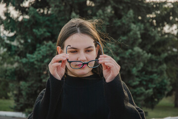 Young woman adjusting glasses in park setting. Glasses for vision