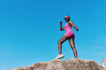 Woman in pink athletic wear poses confidently on a rock against a bright blue sky