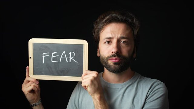 Caucasian Man holding a Chalkboard with the Handwritten word  "fear"
