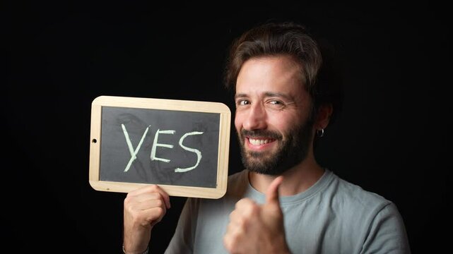 Caucasian Man holding a Chalkboard with the Handwritten word  "yes"