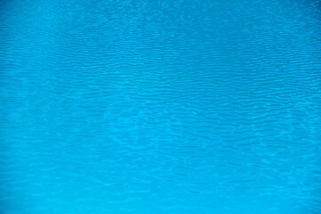 Gentle waves ripple over the water surface under the midday sun in a serene coastal environment.