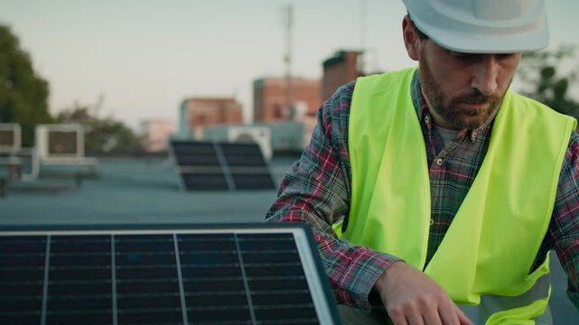 Male engineer in safety gear inspects a solar panel carefully, ensuring its proper alignment and functionality on a rooftop installation. Close up of man worker outdoors.