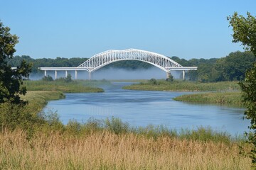 Fototapeta premium White arch bridge spanning the tranquil river in a lush landscape during a clear day