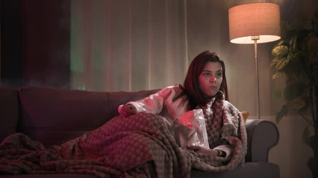 beautiful redhead woman eating potato chips and watching TV series in dark room