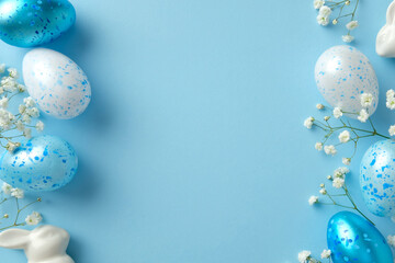 Blue and white speckled Easter eggs with delicate flowers and ceramic bunny on a pastel blue...