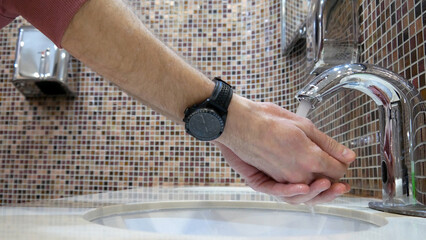 Close-up of a public toilet faucet used by a man to wash his hands
