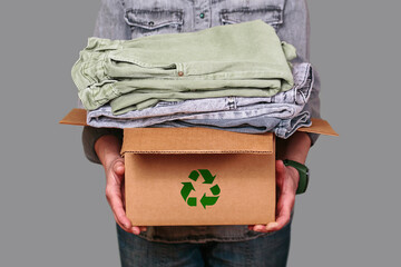 Unrecognizable woman holding a cardboard box filled with secondhand clothes, promoting sustainable...