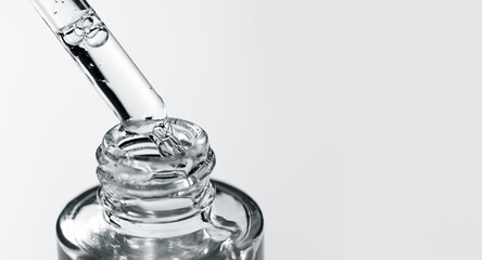 Cosmetic dropper with serum, essential oil, beauty cosmetics dripping, on grey background. Macro shot. Serum, peptides, beauty and health care products. Glass pipette with liquid. Top view. Skin care