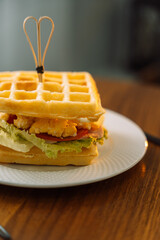 Fresh homemade belgian waffle sandwich with green lettuce, Scrambled eggs, tomato on wooden table