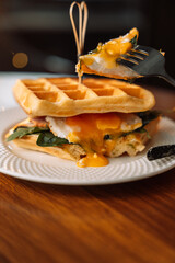 Breakfast homemade belgian waffle sandwich with egg, fork in hand