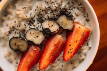 Oatmeal with strawberries in a white bowl on wooden background, close up