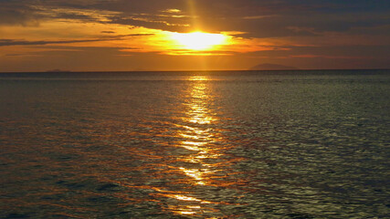 Fototapeta premium Sunset over the sea. View of the calm surface of the ocean during sunset. The sun sets behind the sea behind the clouds.