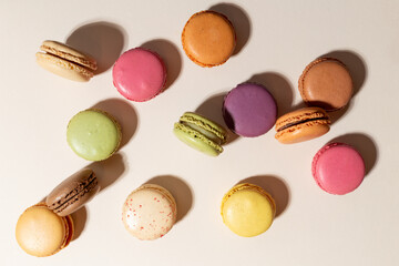 Bunte Macarons stehend und liegend, chaotisch geordnet auf dem beigen Hintergrund. Farbenfrohe, fröhliche Kombination.