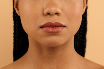 Close-up of young african american woman's lips and lower face with a smooth skin texture and braids visible on both sides, black female standing isolated on beige studio background, cropped