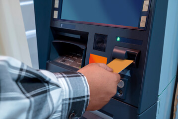 Male hand inserting a bank card into an ATM (Automatic cash machine) to access bank service or...