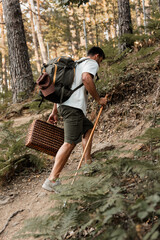 Adult man climbing a forest trail with a backpack and walking stick