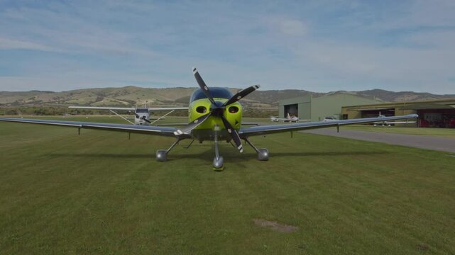 Front Green JMB VL3 Ultralight Private Aircraft Aviation Parked at Regional Airstrip on Grass Blue Sky Clouds Wide Shot