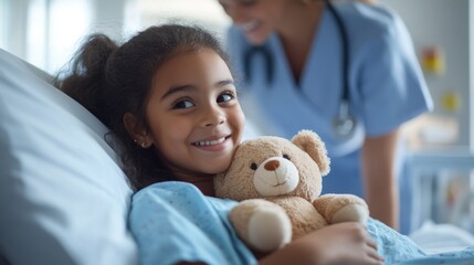 Hispanic female child smiling in hospital bed holding teddy bear with nurse in background