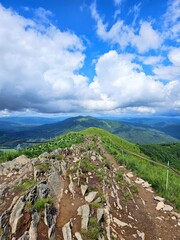 Hiking trail on Połonina Caryńska, Bieszczady, Poland, with grassy meadows and distant mountains under a partly cloudy sky.