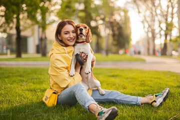 Fototapeta premium Cheerful woman enjoying time with her dog outdoors in a green park during a sunny day.