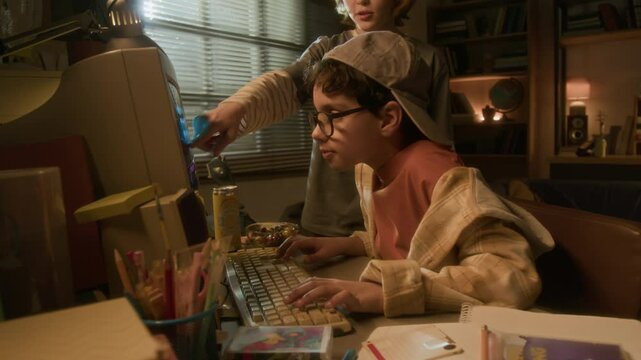 Side view zoom in shot of two young boys using retro computer together with friend pointing at screen in warm toned 90s setting