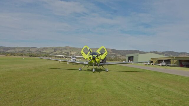 Front Green JMB VL3 Ultralight Private Aircraft Aviation Parked at Regional Airstrip on Grass Blue Sky Clouds Wide Shot