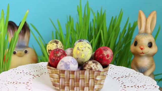 A basketful with colorful eggs and two toy hares in the grass